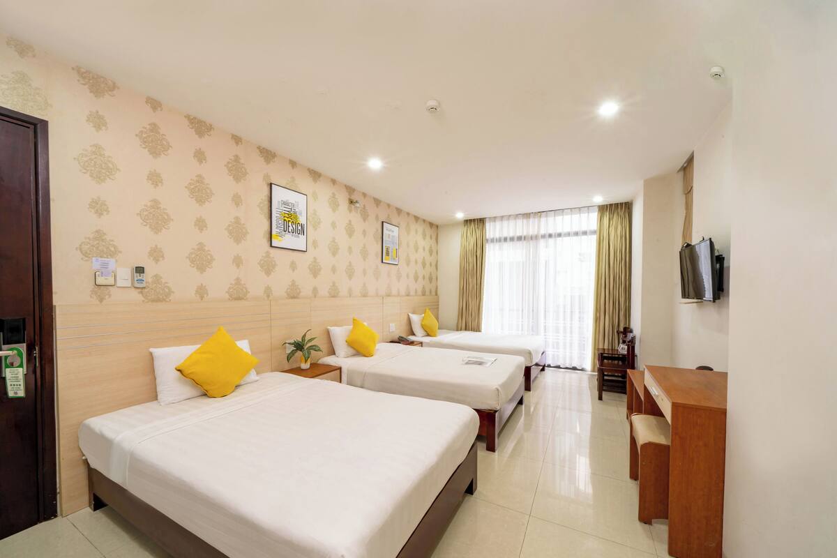 A hotel room with three beds, a desk, a television, and a window with curtains.