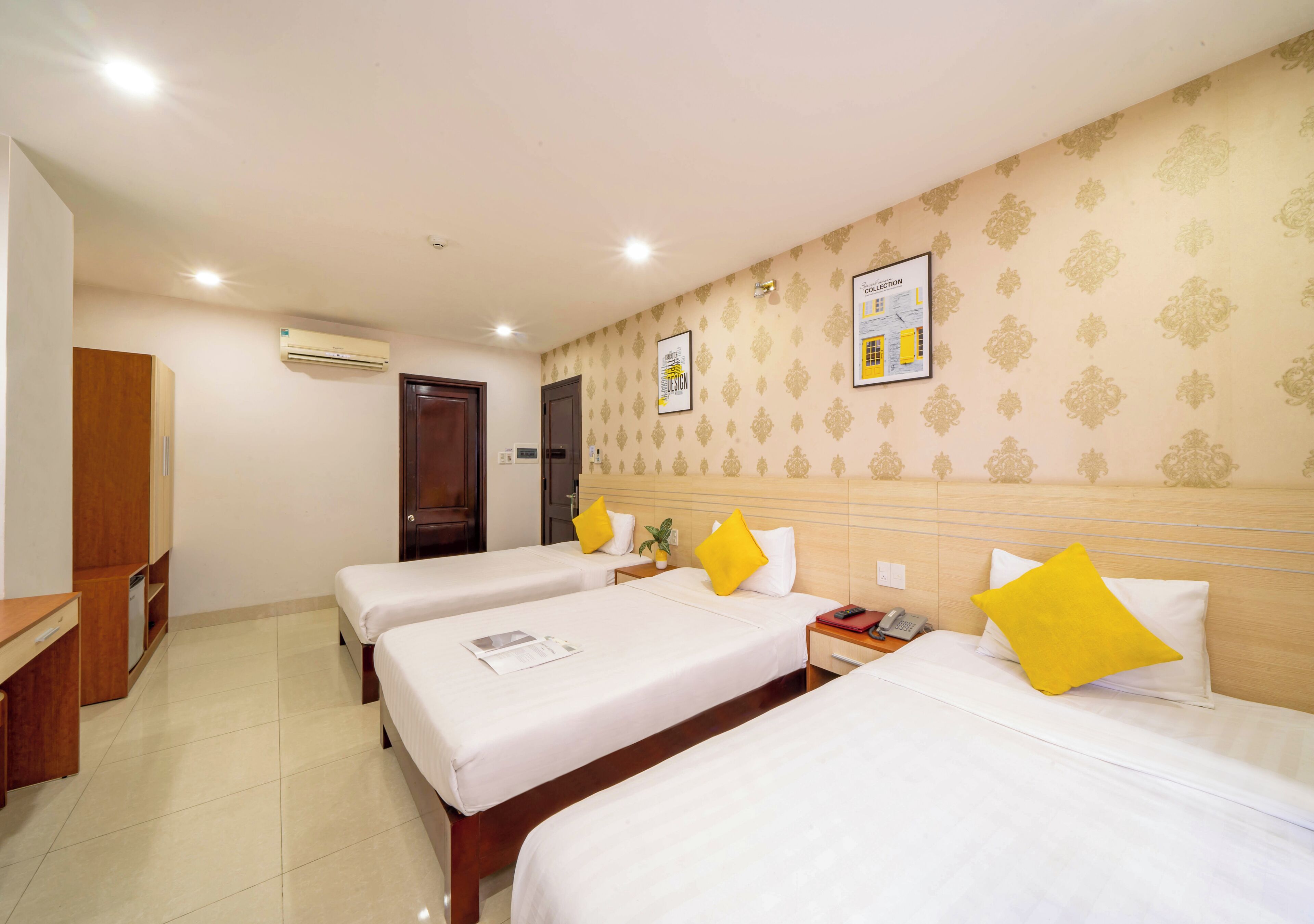 A hotel room with three single beds, a wooden headboard, a desk, and a wardrobe.