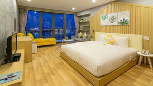 A modern hotel room with a large bed, a desk, a sofa, and a view of the cityscape at night. - Happy Day Riverside Hotel & Spa Danang (Da Nang)