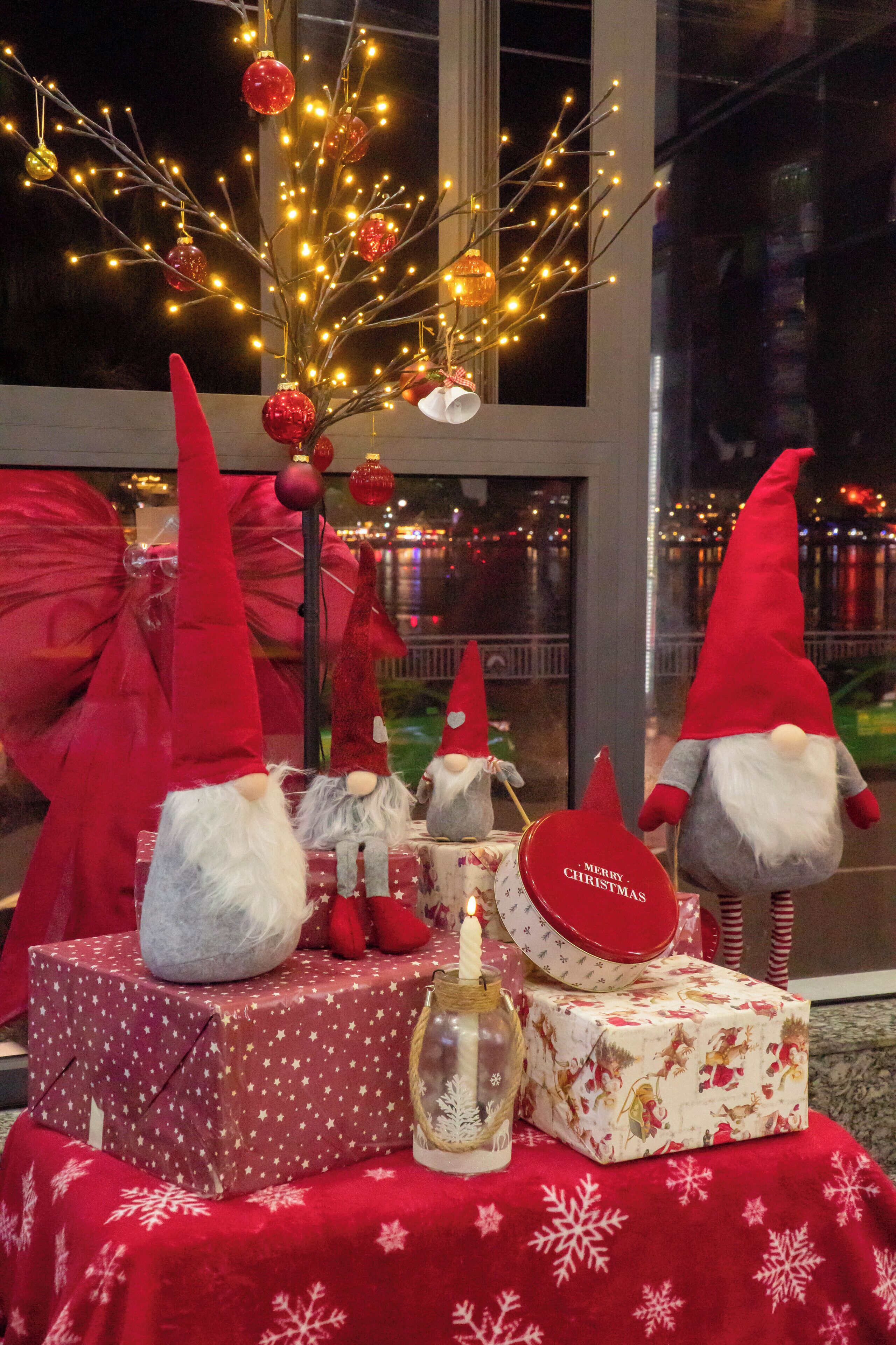 Une décoration festive avec des figurines de lutins, des cadeaux emballés et un sapin de Noël orné de guirlandes lumineuses et de décorations.