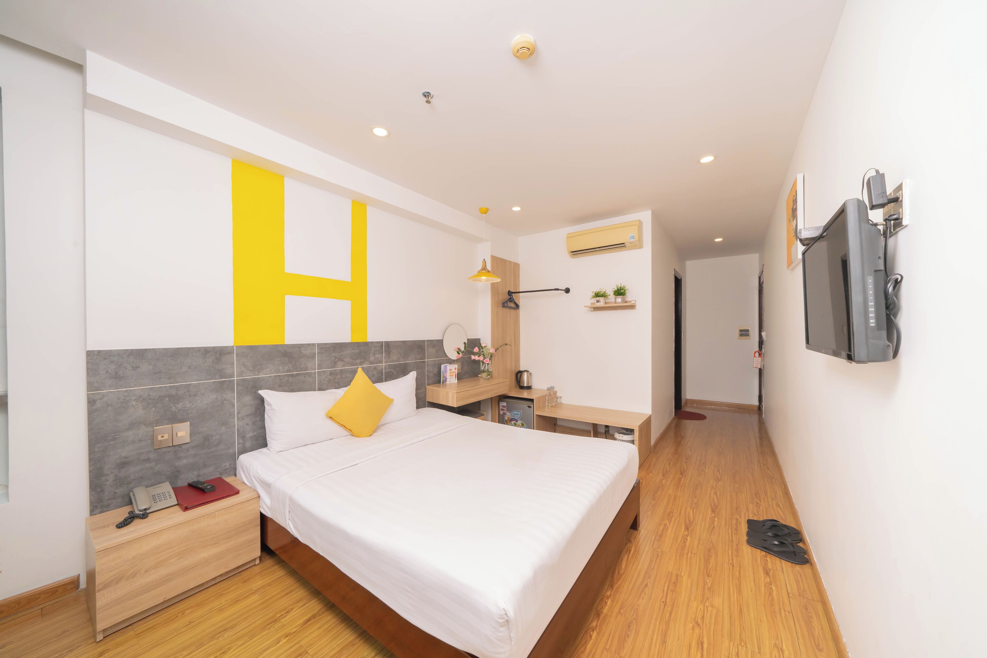 A modern hotel room with a large bed, bedside table, and a TV mounted on the wall.