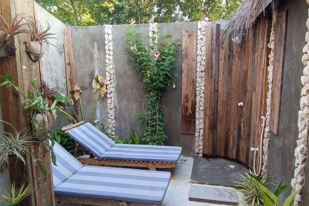A small outdoor patio with two striped lounge chairs, a concrete wall, and a wooden fence with stone accents.