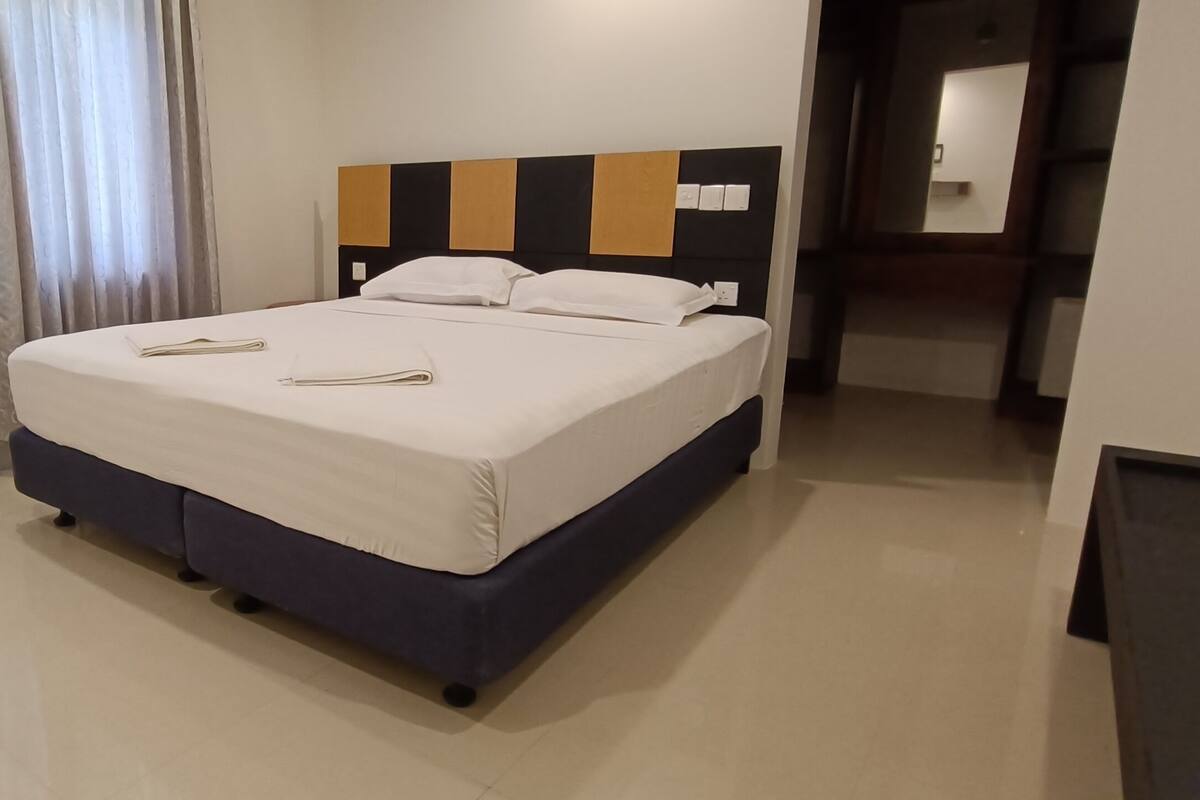 A modern hotel room with a large bed, a headboard with a geometric pattern, and a neutral color scheme.