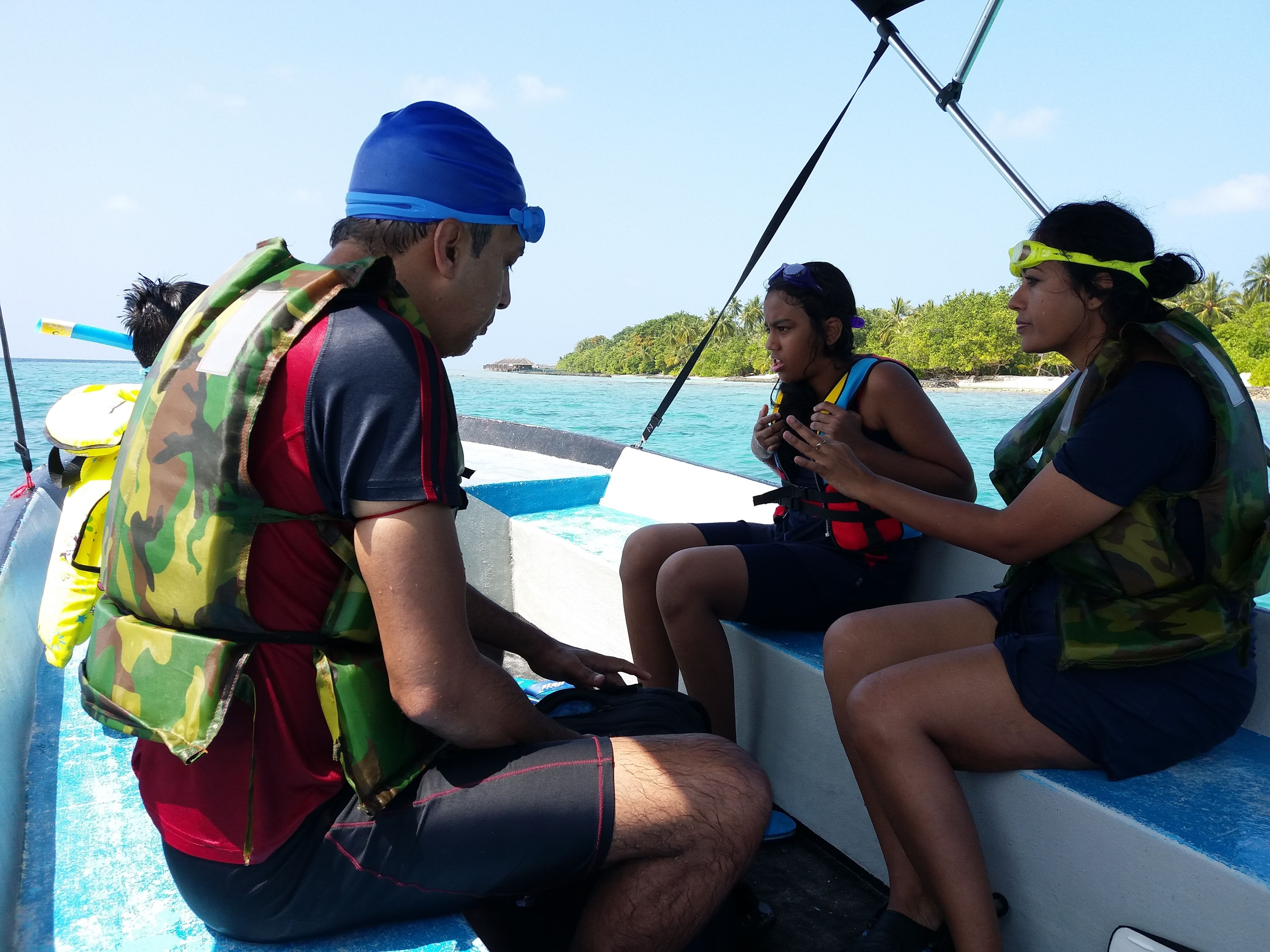 Three people on a boat wearing life jackets, with a clear view of the ocean and distant shoreline.