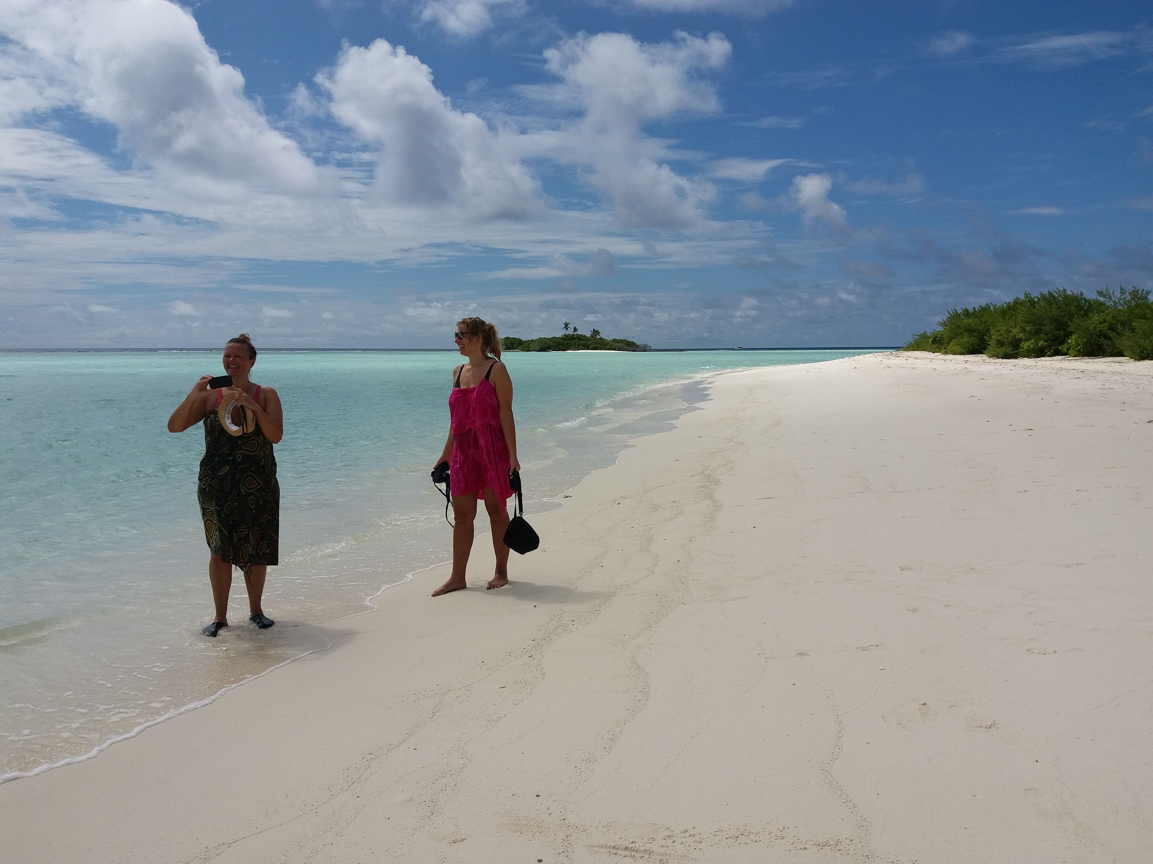A beach with two people, one taking a photo, and another holding a camera.