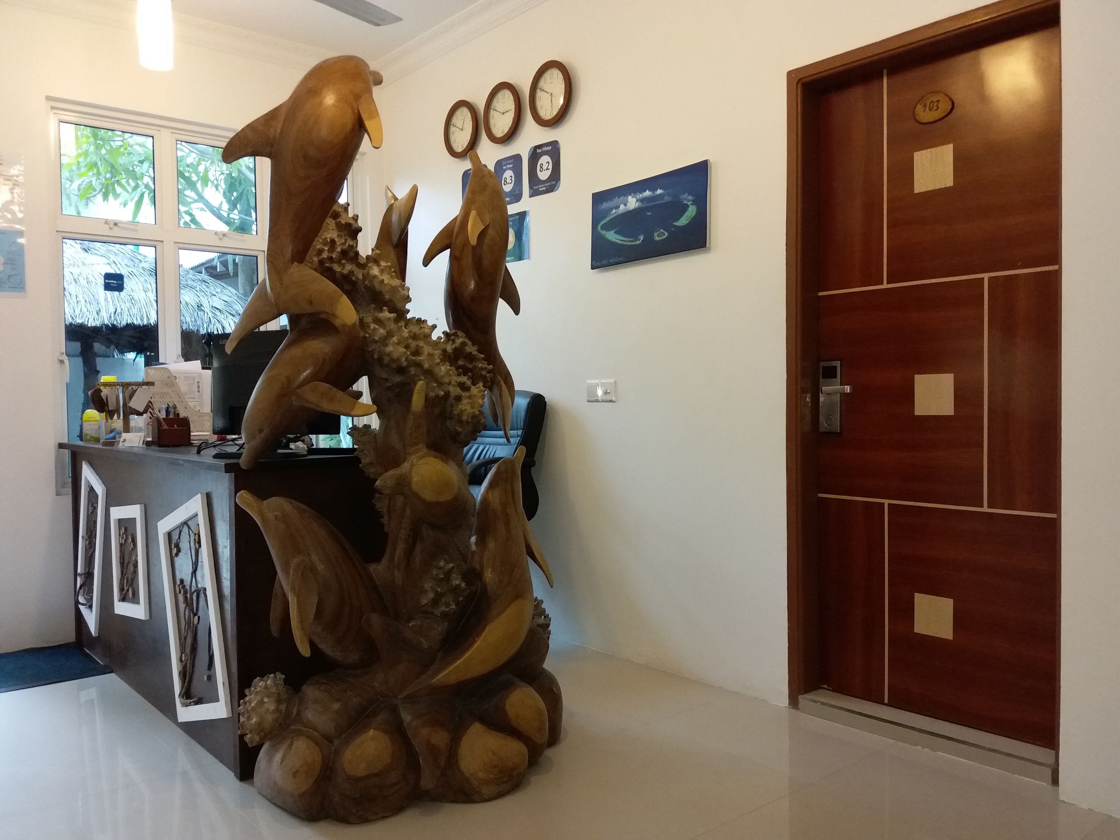 A reception desk with a large wooden sculpture, a clock, and a door with a number plate.