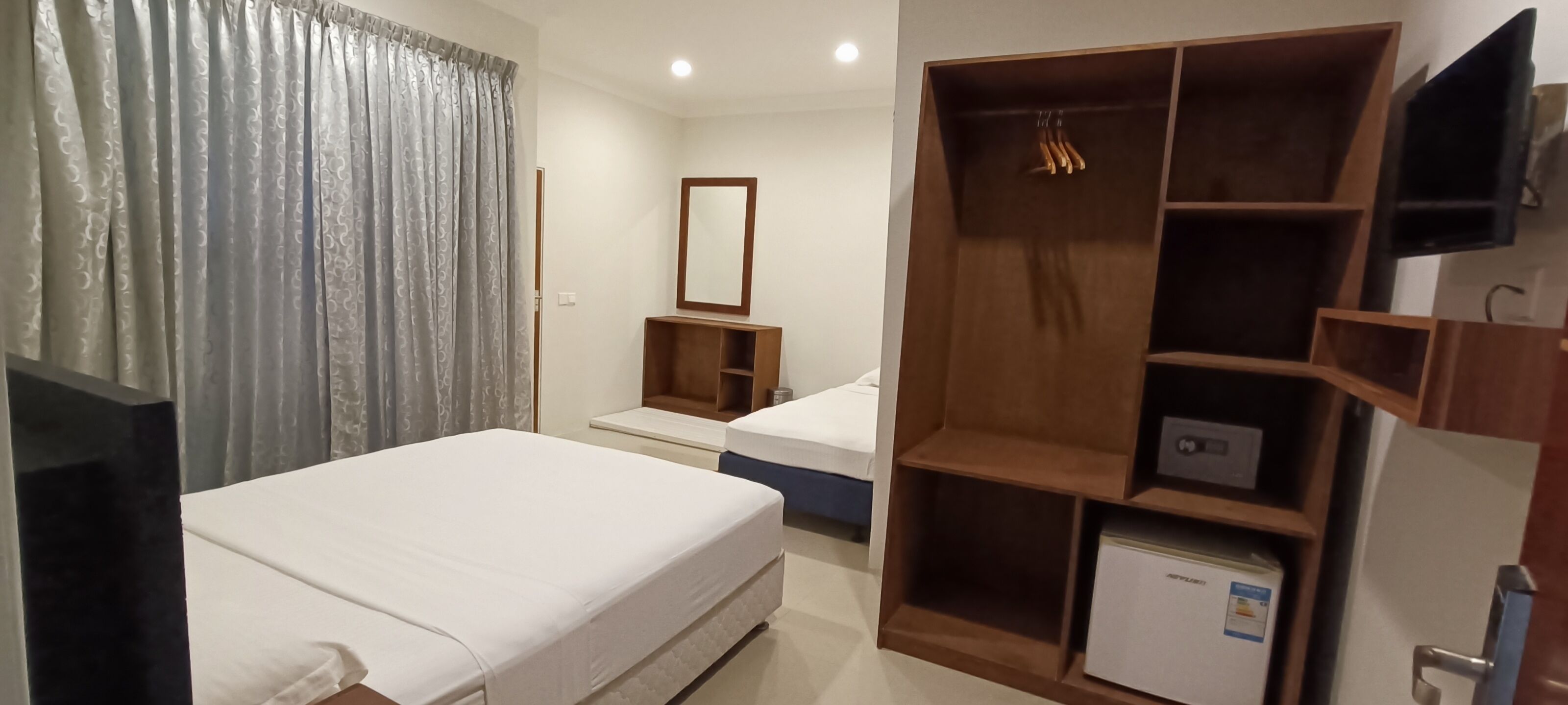 Una habitación de hotel con cama, armario, espejo y un refrigerador pequeño.