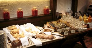 Ein Buffet mit verschiedenen Speisen, darunter Backwaren und Brot, sowie einer Auswahl an Soßen und Getränken.
