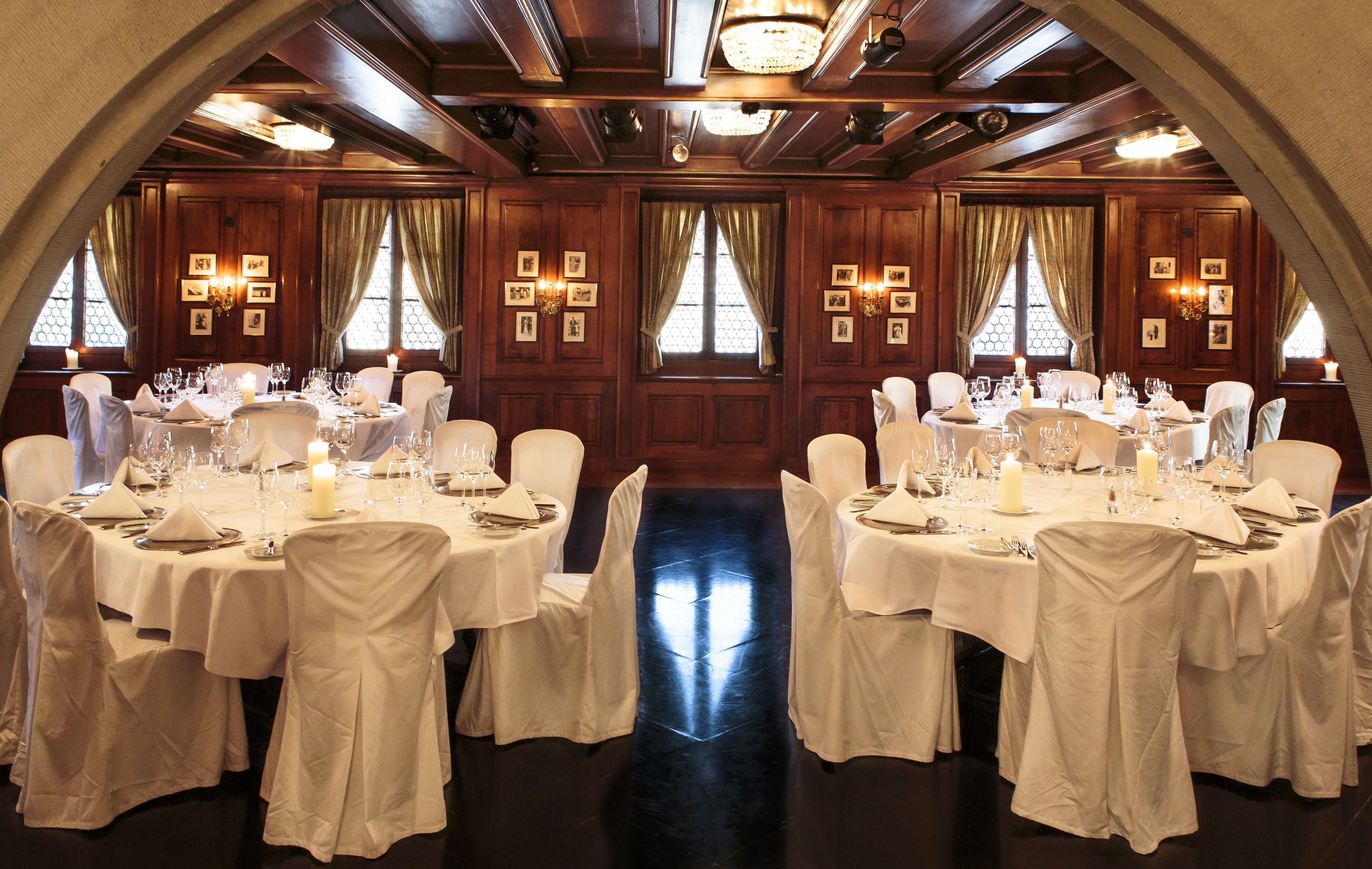 Un salón de banquetes con mesas redondas dispuestas para comer, paneles de madera y candelabros.