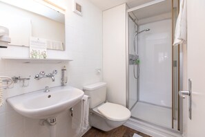 Ein Badezimmer mit weißem Waschbecken, WC und Duschkabine aus Glas.