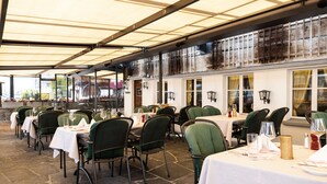 A restaurant with outdoor seating under a covered area, featuring tables with white tablecloths and green chairs. - Swiss-Chalet Merlischachen - Historik Chalet-Hotel Lodge (Kuessnacht)