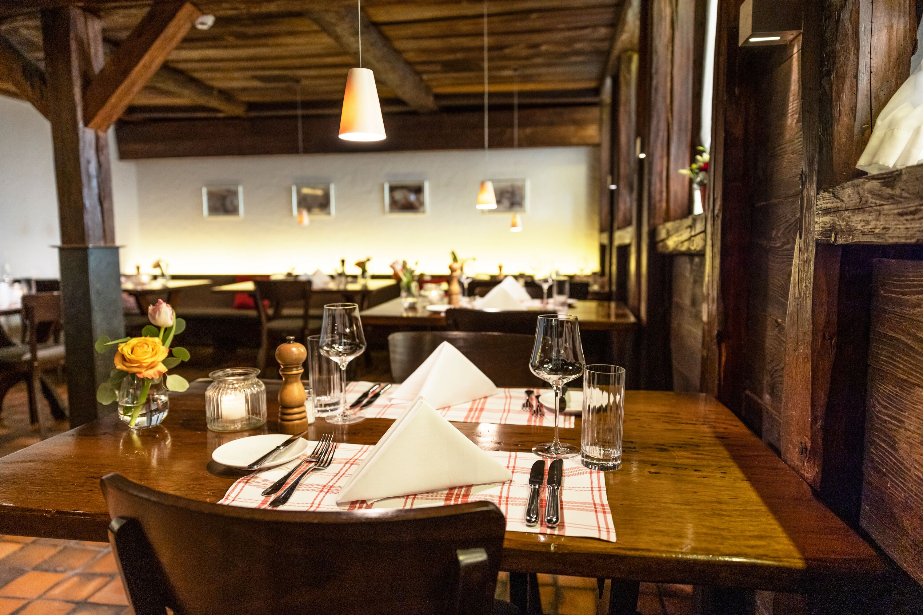 A restaurant with wooden tables set for dining, featuring a checkered tablecloth, wine glasses, and cutlery.