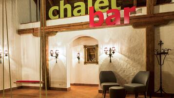 A chalet bar with wooden beams, a red bench, and two chairs.