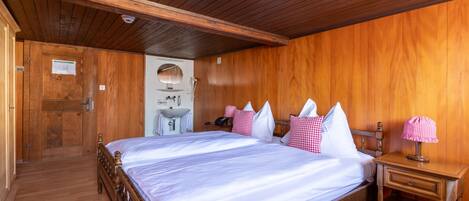 Un dormitorio con paneles de madera, una cama grande, una mesita de noche, un espejo y una puerta que da a otra habitación.