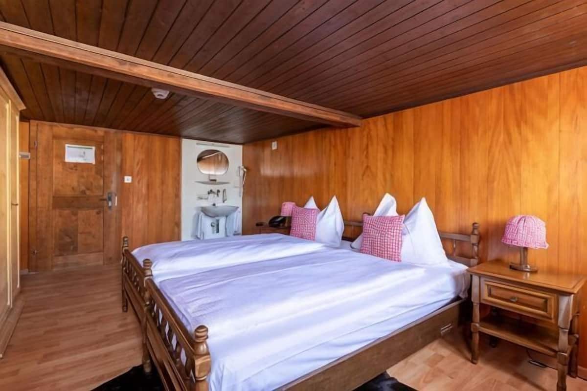 Une chambre aux murs lambrés, avec un grand lit, une table de chevet, un miroir et un lavabo.