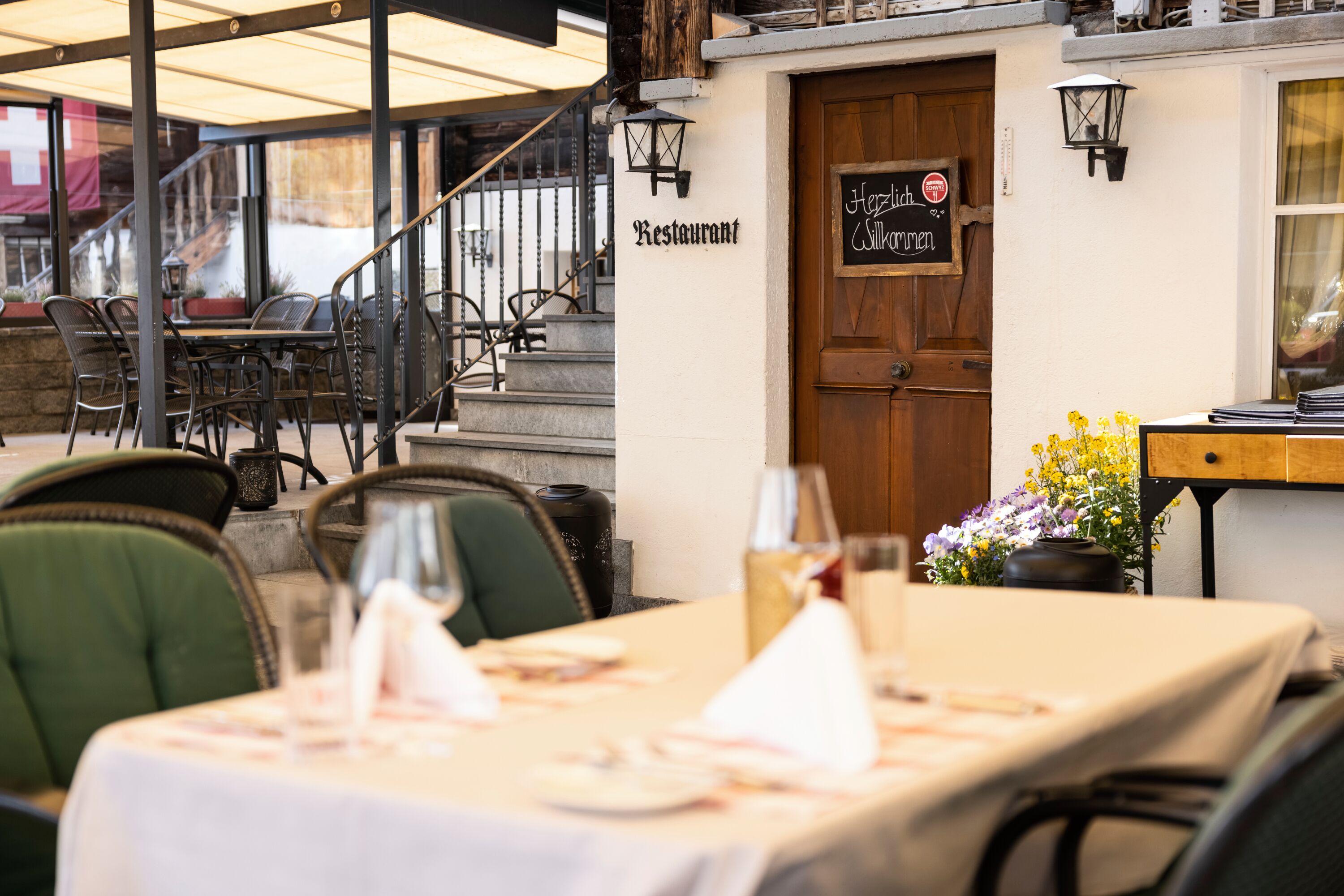 Un restaurante al aire libre con puerta de madera, un letrero que dice 'Restaurant' y una mesa dispuesta con una botella y vasos.