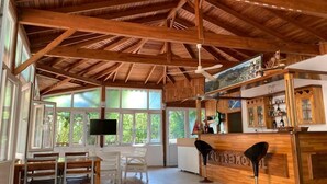 Una habitación amplia con un alto techo de madera, una zona de bar con mostrador y un área de estar con sillas y una mesa.