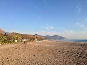 Ein Strand mit einer Holzkonstruktion, blauem Himmel und Bergen im Hintergrund.