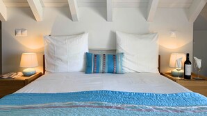 A neatly made bed with white and blue bedding, two bedside lamps, and a bottle of wine on the nightstand. - Residence Lagos (Lagos)