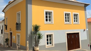 A yellow building with white windows and a brown door, featuring a small balcony and potted plants. - Residence Lagos (Lagos)