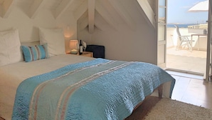 A bedroom with a large bed, a nightstand, a chair, and a view of the sea through a glass door. - Residence Lagos (Lagos)