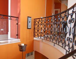 A staircase with ornate metal railings, a white wall, and a floor lamp.