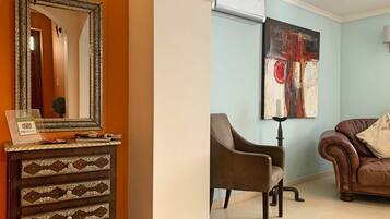 A living room with a brown leather sofa, a brown armchair, a wooden cabinet with drawers, a large mirror, and a modern air conditioning unit.