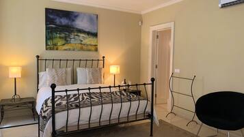 A bedroom with a bed, two bedside tables, a chair, a painting, and a door.