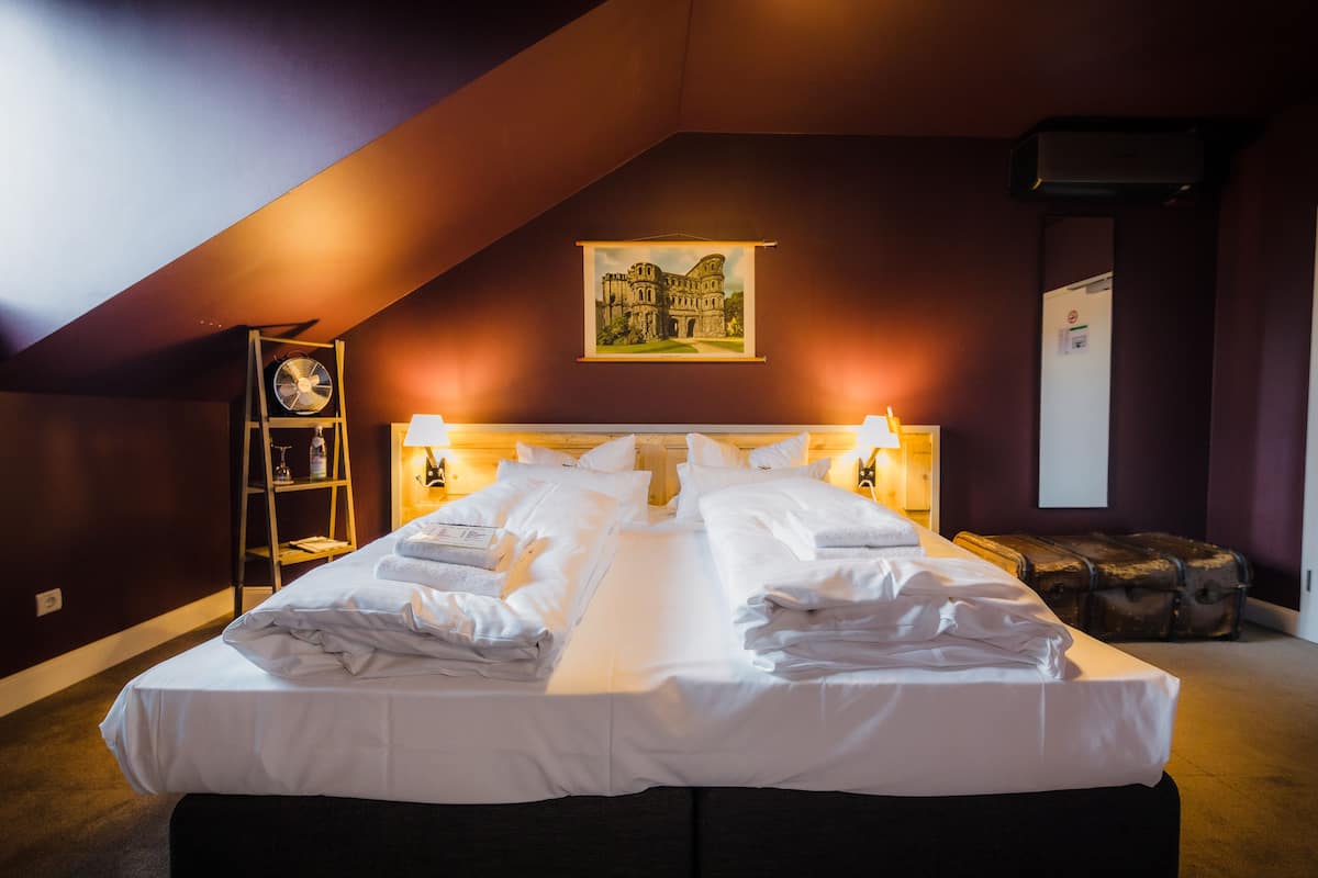 A hotel room with a large bed, two bedside tables, a wall-mounted picture, a ceiling fan, and a suitcase.