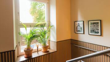 Una escalera con barandilla, una ventana con plantas y cuadros en la pared.