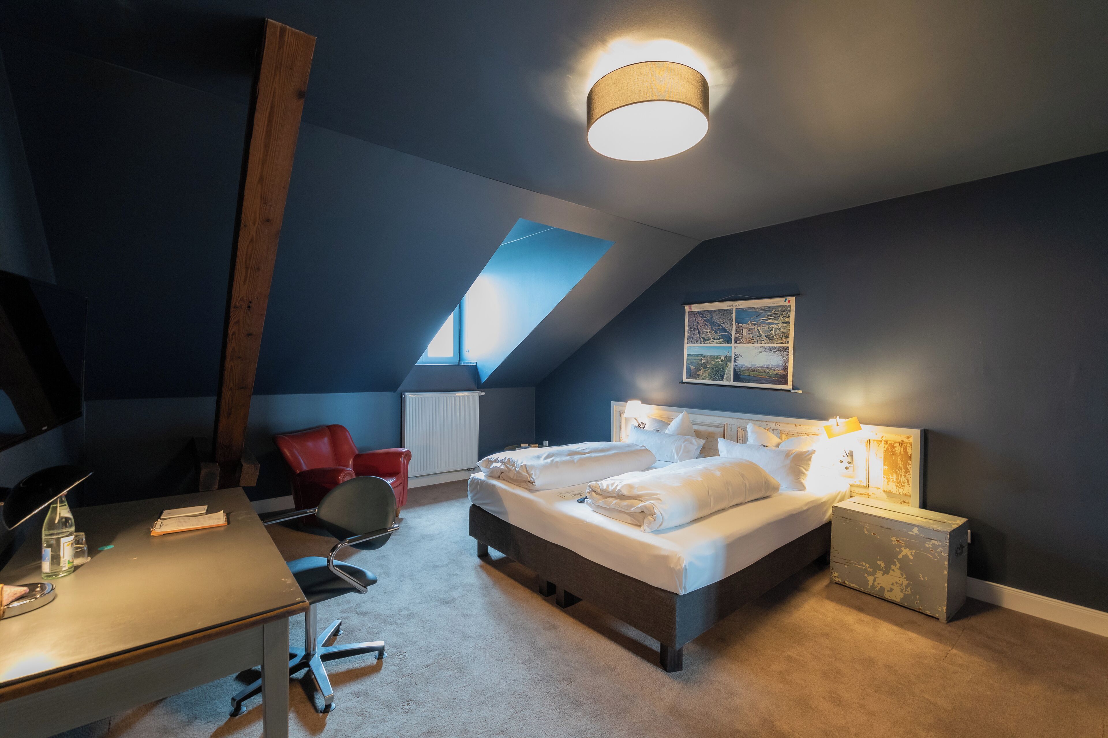 A bedroom with a bed, a desk, a chair, a radiator, and a window.
