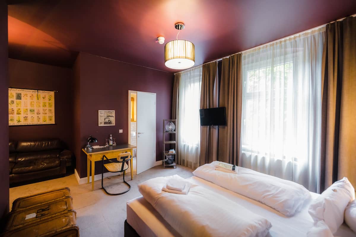 A hotel room with a bed, a desk, a chair, a television, and a window with curtains.