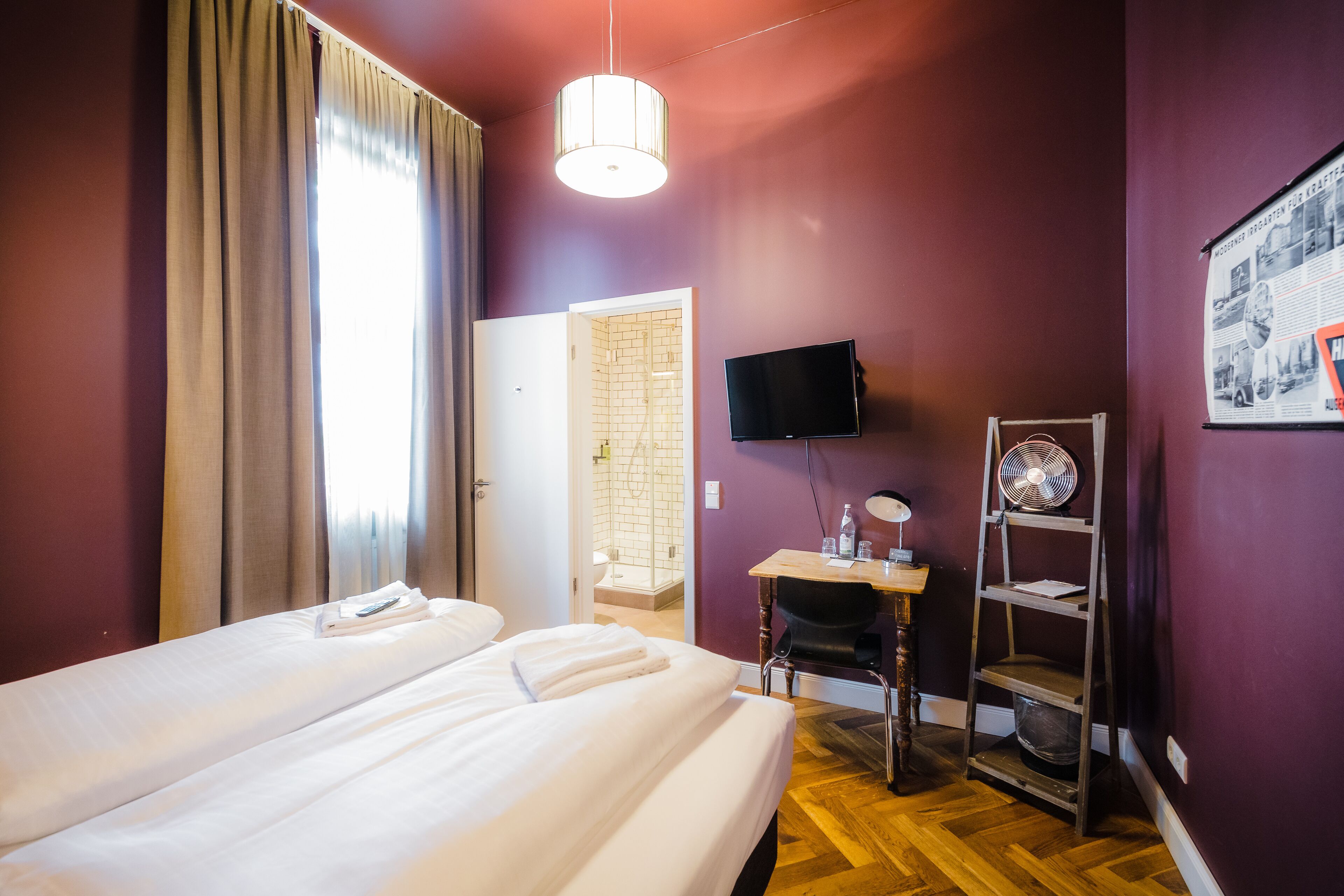 Una habitación de hotel con dos camas, un escritorio, una silla, un televisor y un ventilador.
