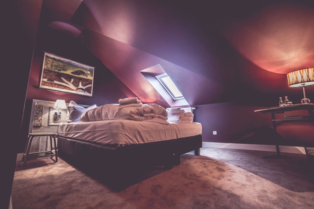 A bedroom with a bed, a desk, a lamp, and a painting on the wall.
