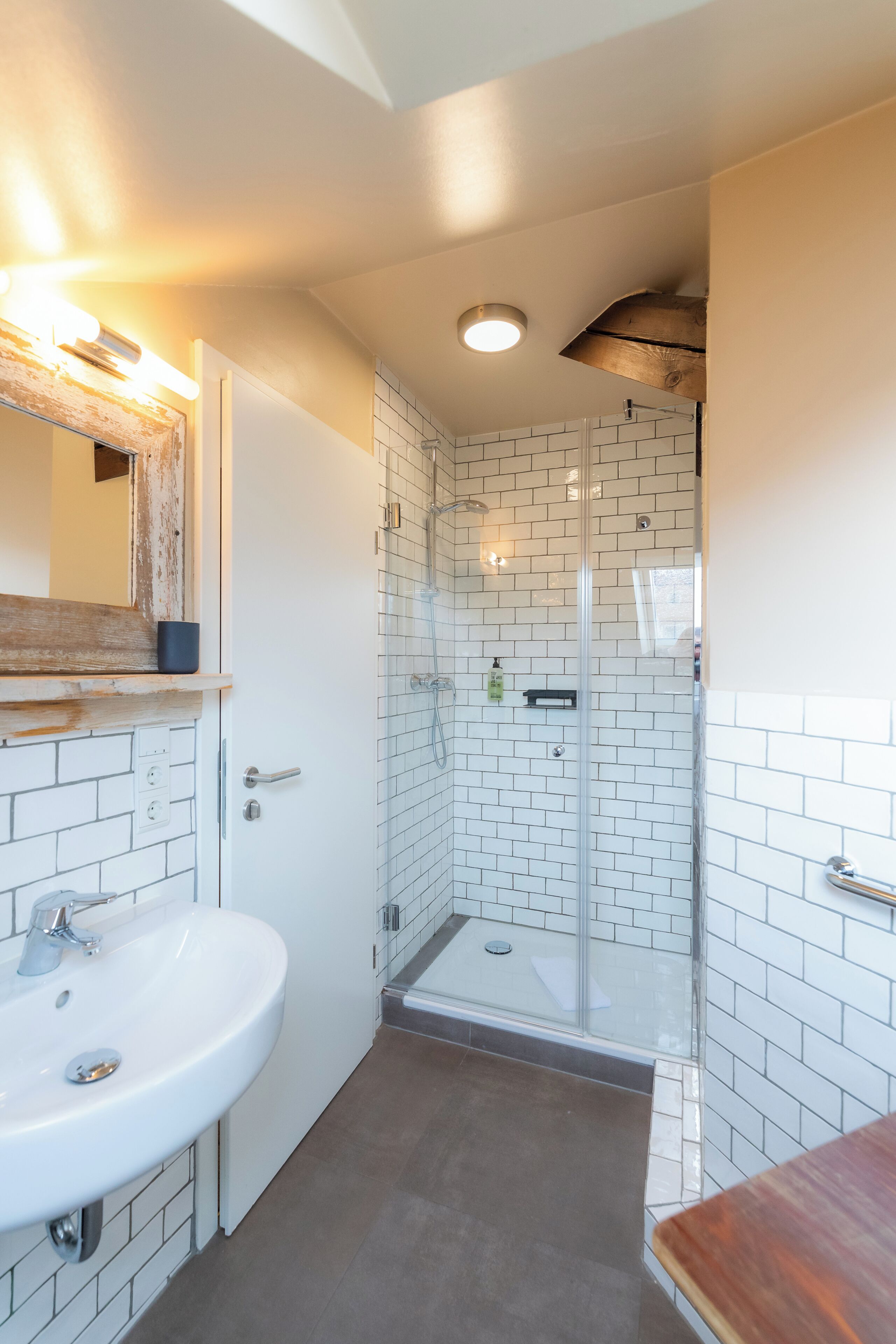 Een badkamer met een witte wastafel, een spiegel, een douche met glazen deuren en een houten plank.