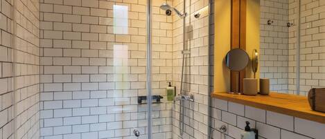 Un baño moderno con paredes de azulejos blancos, cabina de ducha de vidrio, lavamanos blanco y un espejo encima.