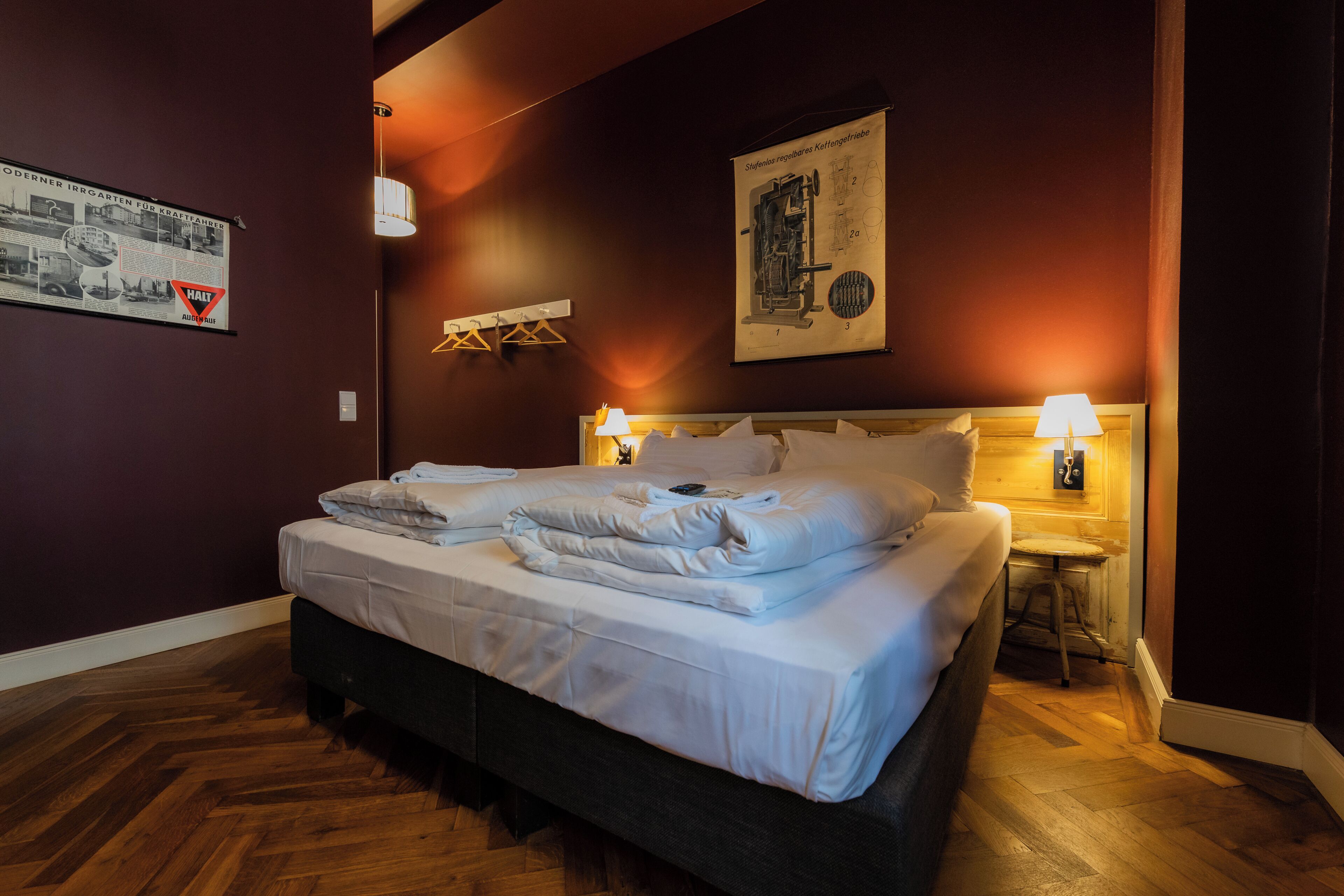 Une chambre d’hôtel avec un lit, deux lampes de chevet, un plancher en bois et une affiche au mur.