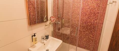 A bathroom with a glass-enclosed shower, a sink with a mirror above it, and a tiled wall.