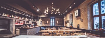 Un bar con pared de ladrillo, mesas de madera y lámparas colgantes.