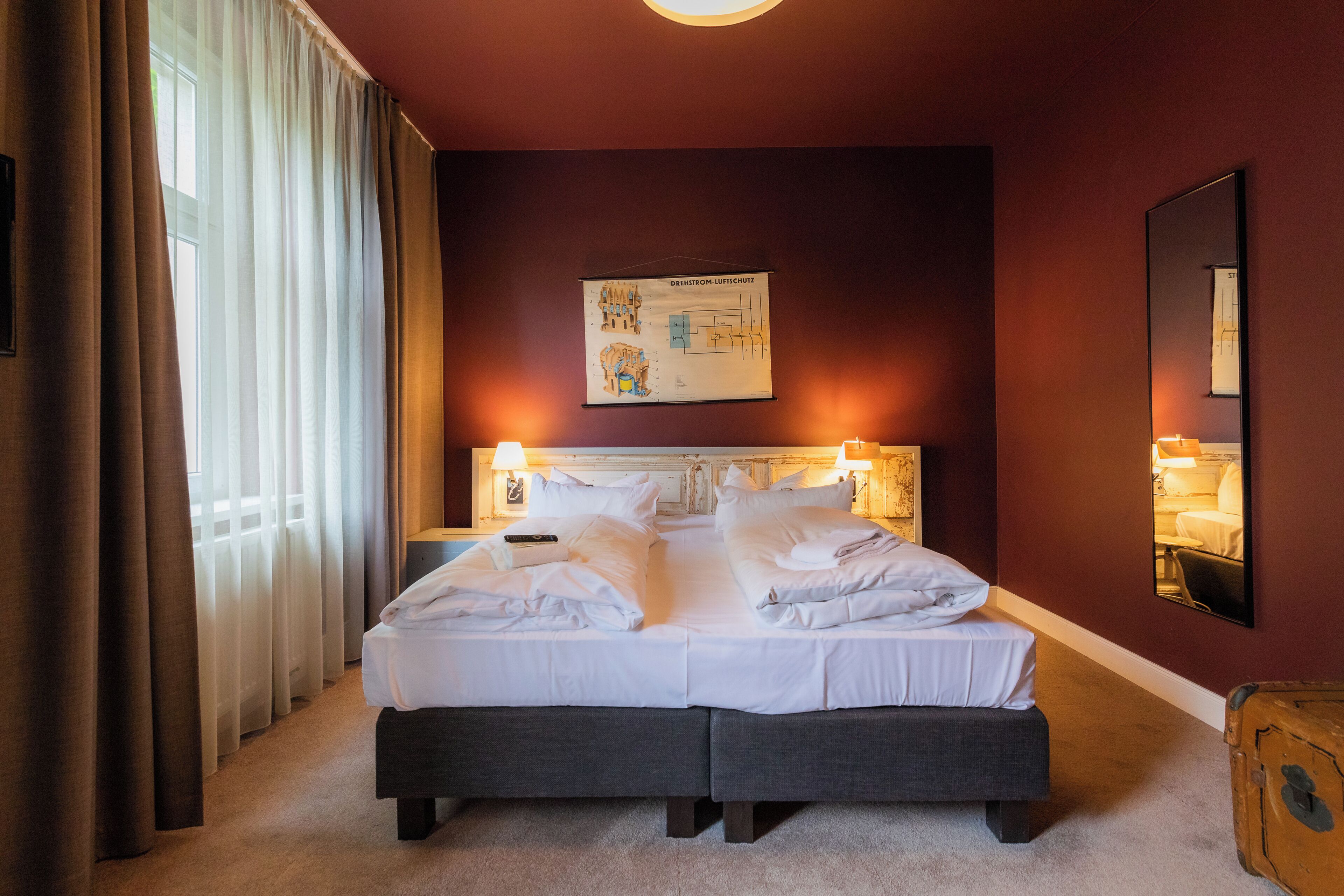 A hotel room with a large bed, a headboard with a light fixture, a wall-mounted artwork, and a suitcase on the floor.