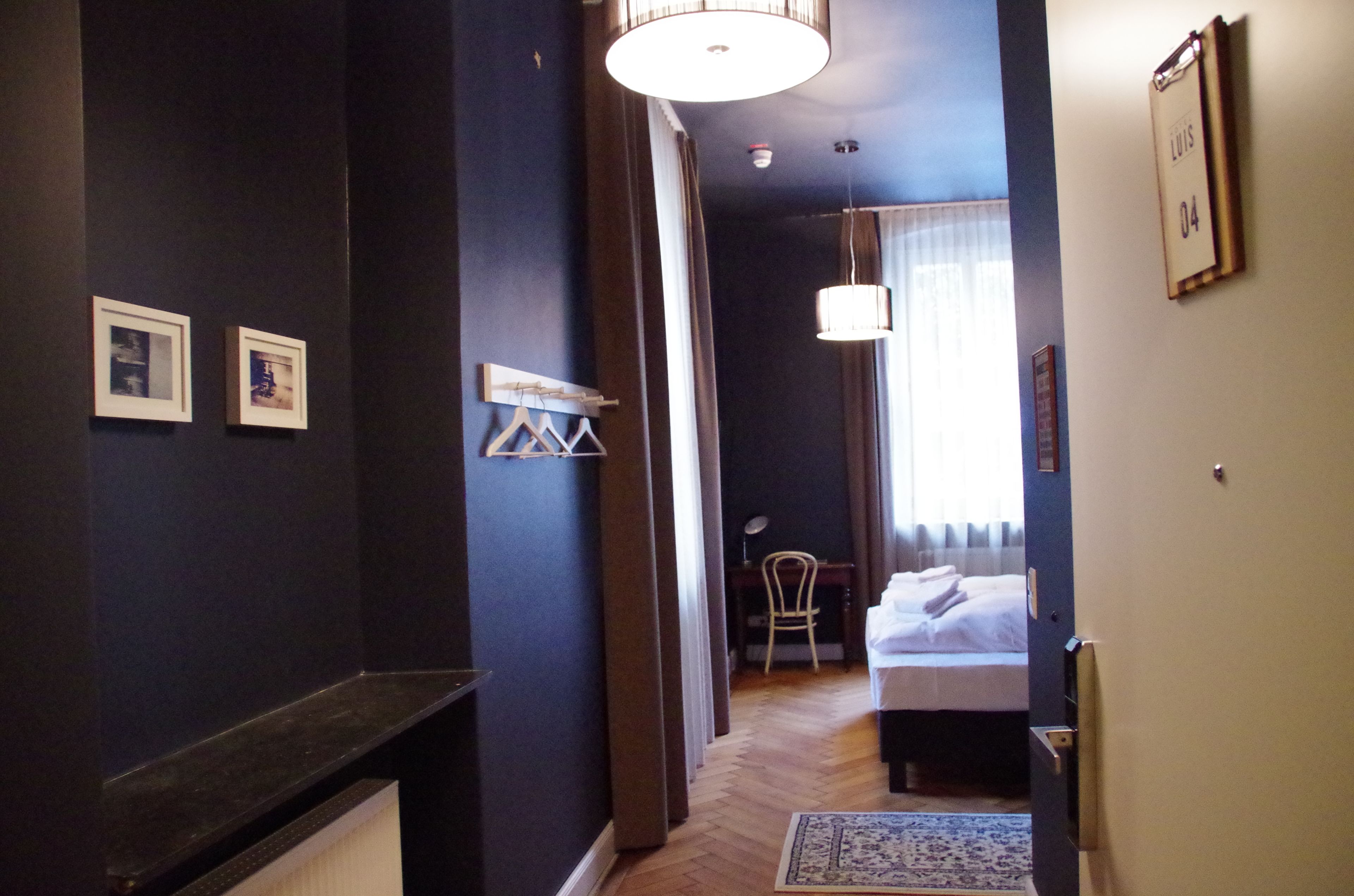 Un couloir d’hôtel avec un lit, un bureau et une chaise. Des tableaux encadrés ornent le mur.