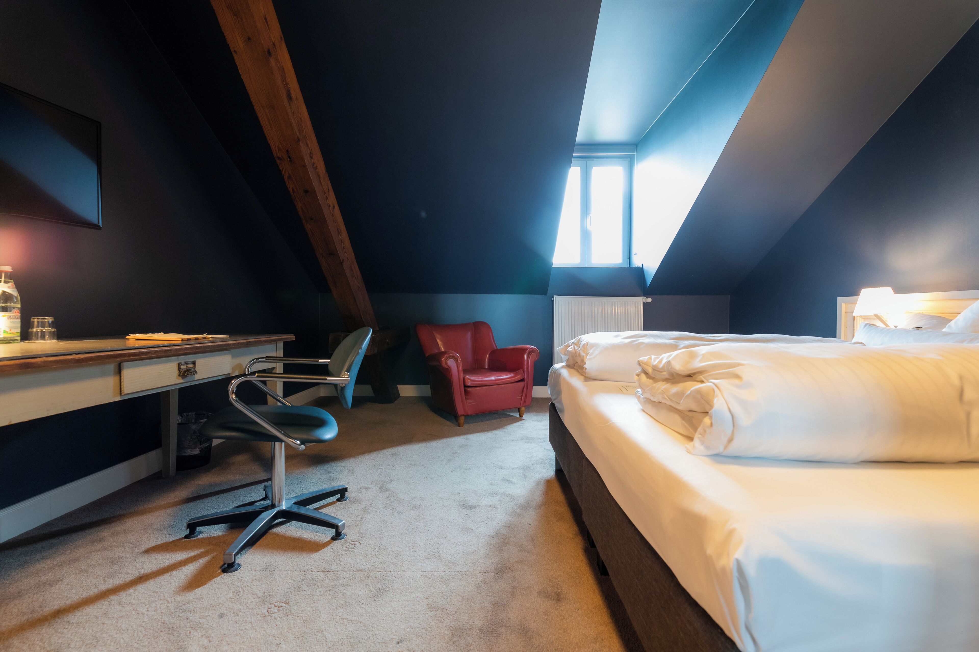 A room with a bed, desk, chair, and a red chair.