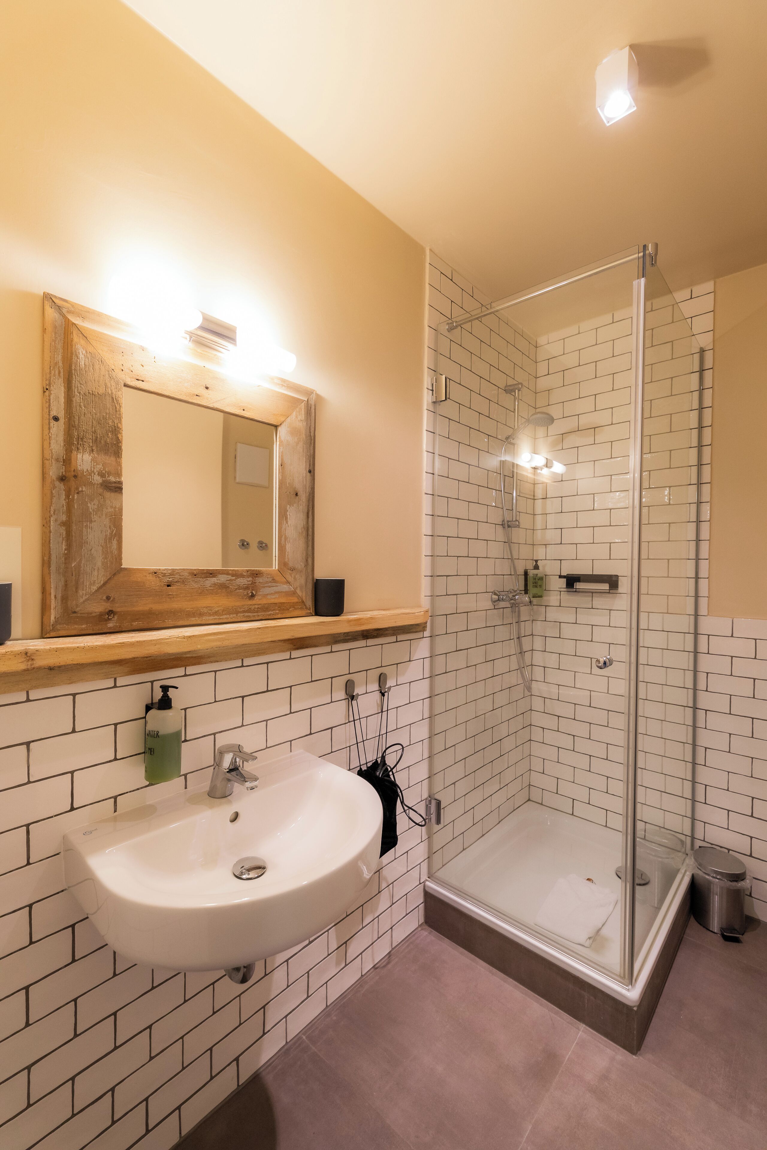 Un baño con un lavabo blanco, un espejo con marco de madera y una ducha con cerramiento de vidrio.