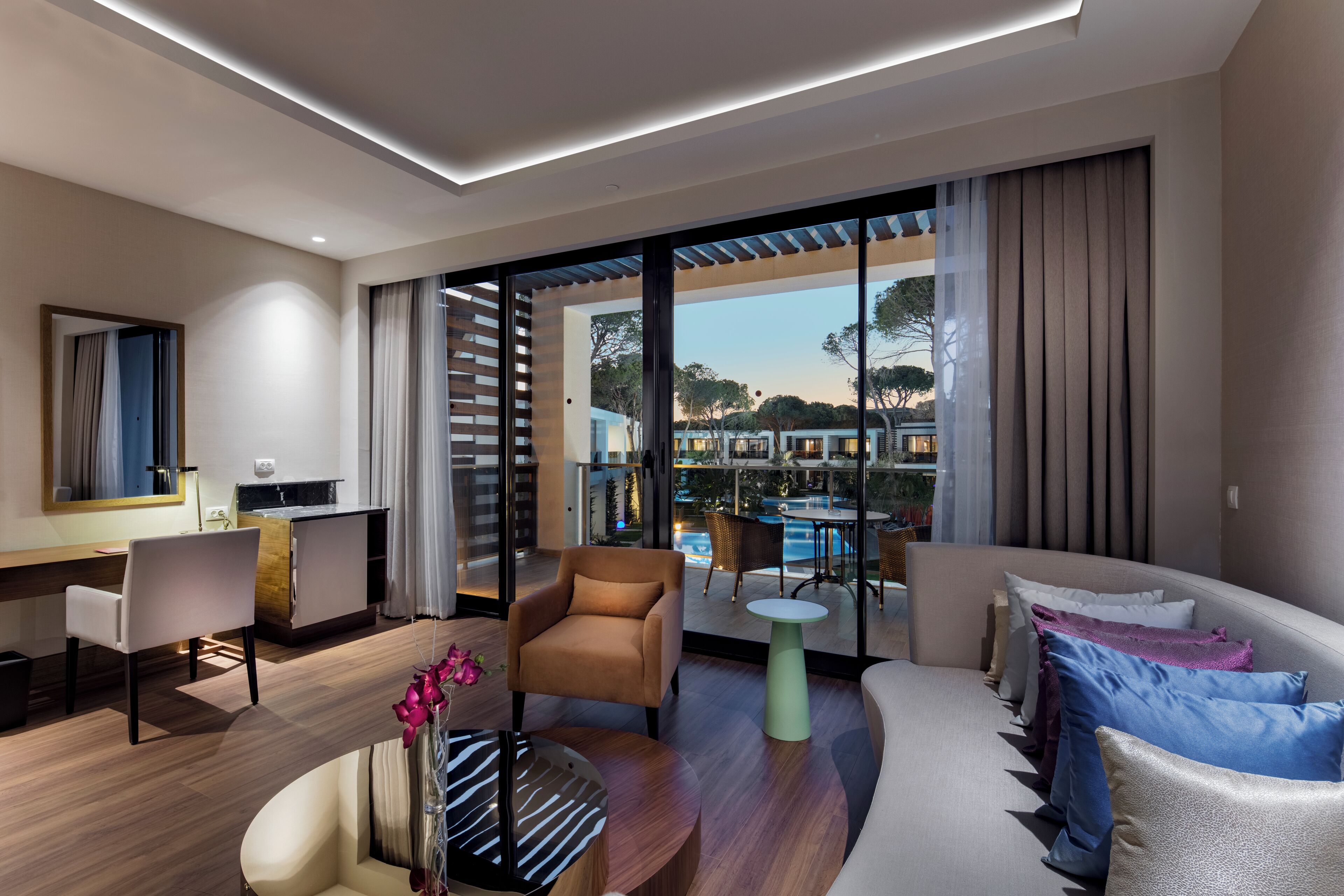 Ein modernes Hotelzimmer mit Balkon, einer Couch, einem Sessel, einem kleinen Tisch und einem Schreibtisch.