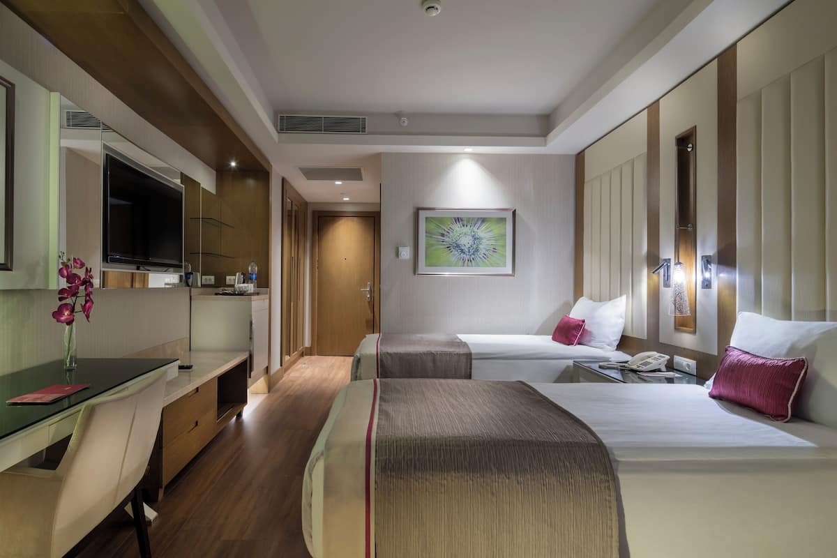A hotel room with a desk, two beds, a TV, and artwork on the walls.