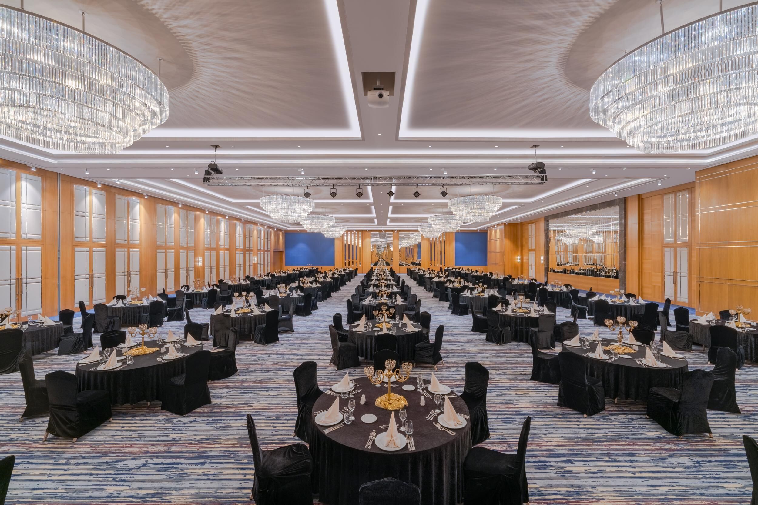 Un amplio salón de banquetes con varias mesas redondas dispuestas para comer, con candelabros y un suelo cubierto de alfombra azul.