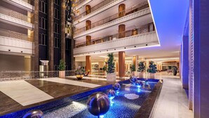 Eine großzügige Hotelhalle mit einem zentralen Wasserspiel und moderner Einrichtung, über mehrere Etagen.