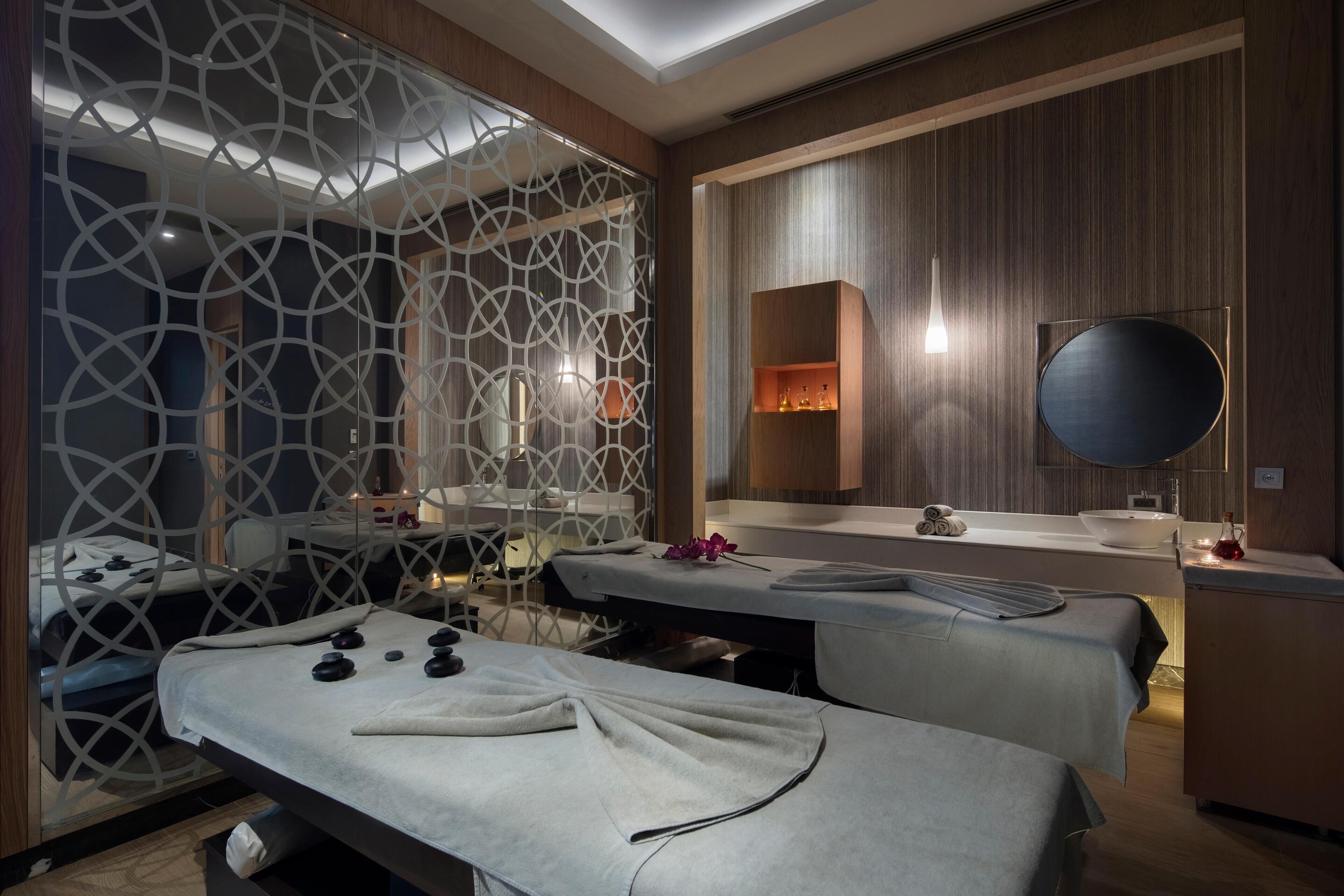 Un spa moderno con una camilla de masaje, un muro decorativo con patrones geométricos, un panel de madera y un espejo redondo.