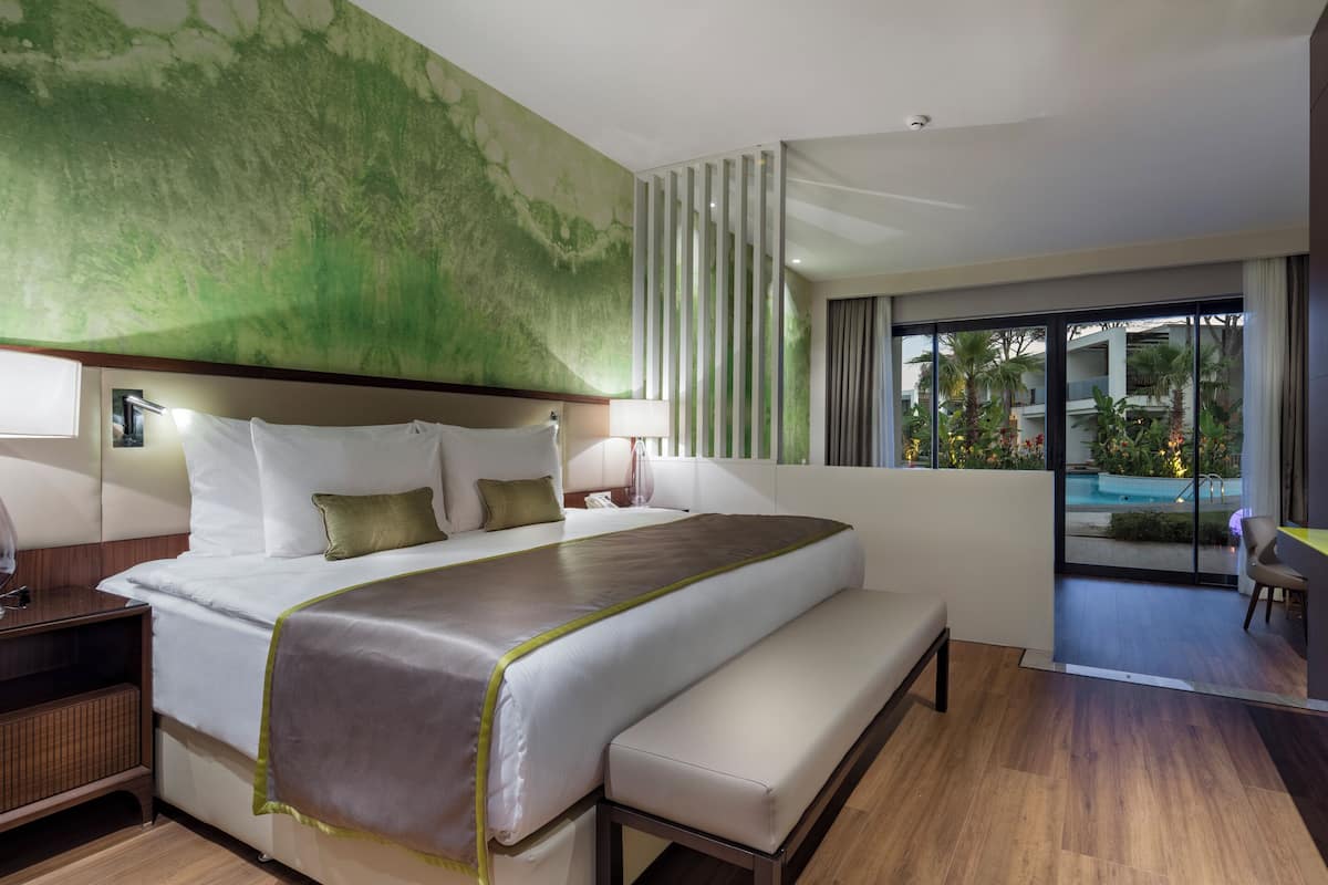 A modern hotel room with a large bed, a desk, and a view of a pool and outdoor area.