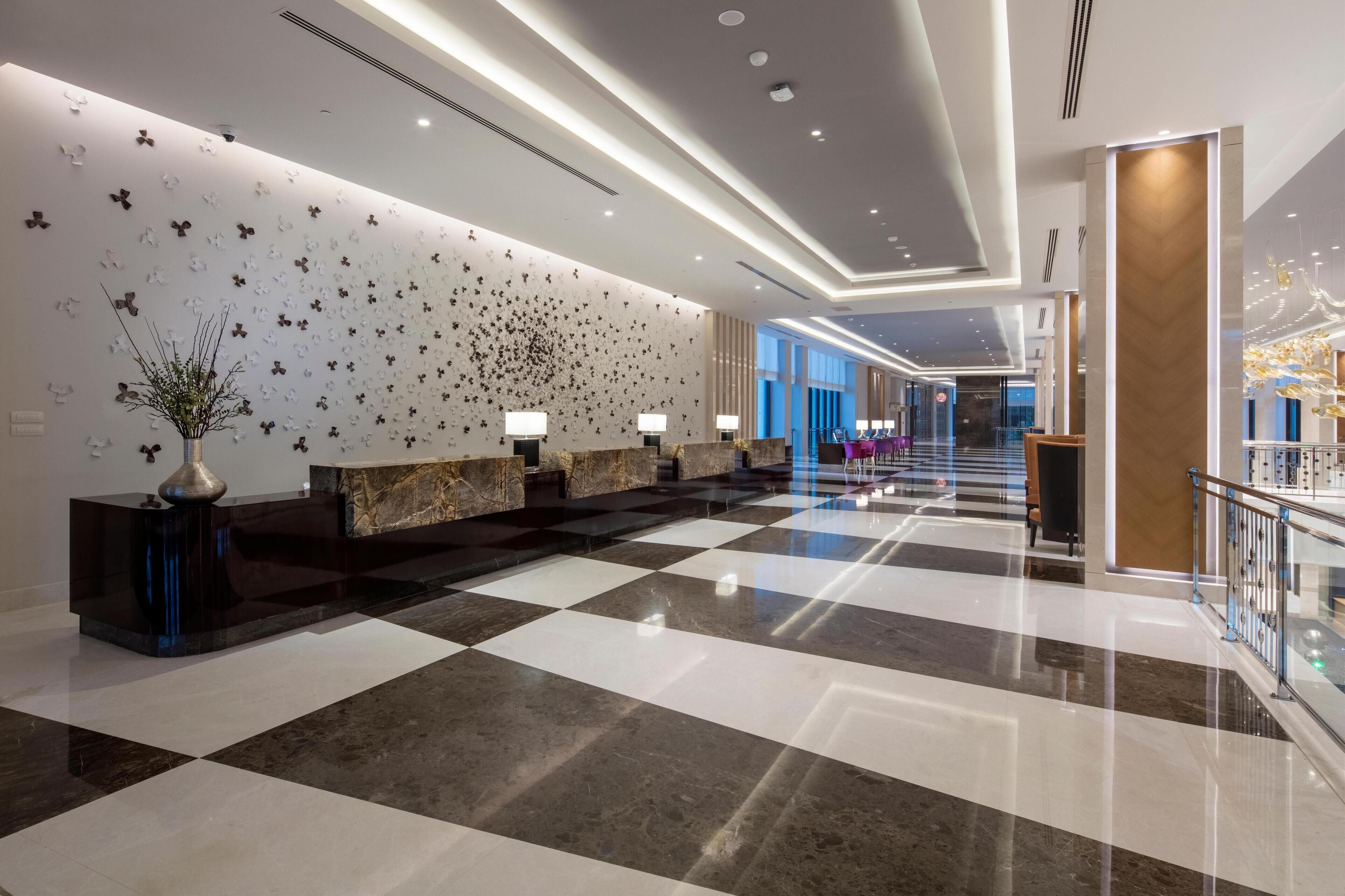 A modern hotel lobby with a checkered floor, a reception desk, and a decorative wall.